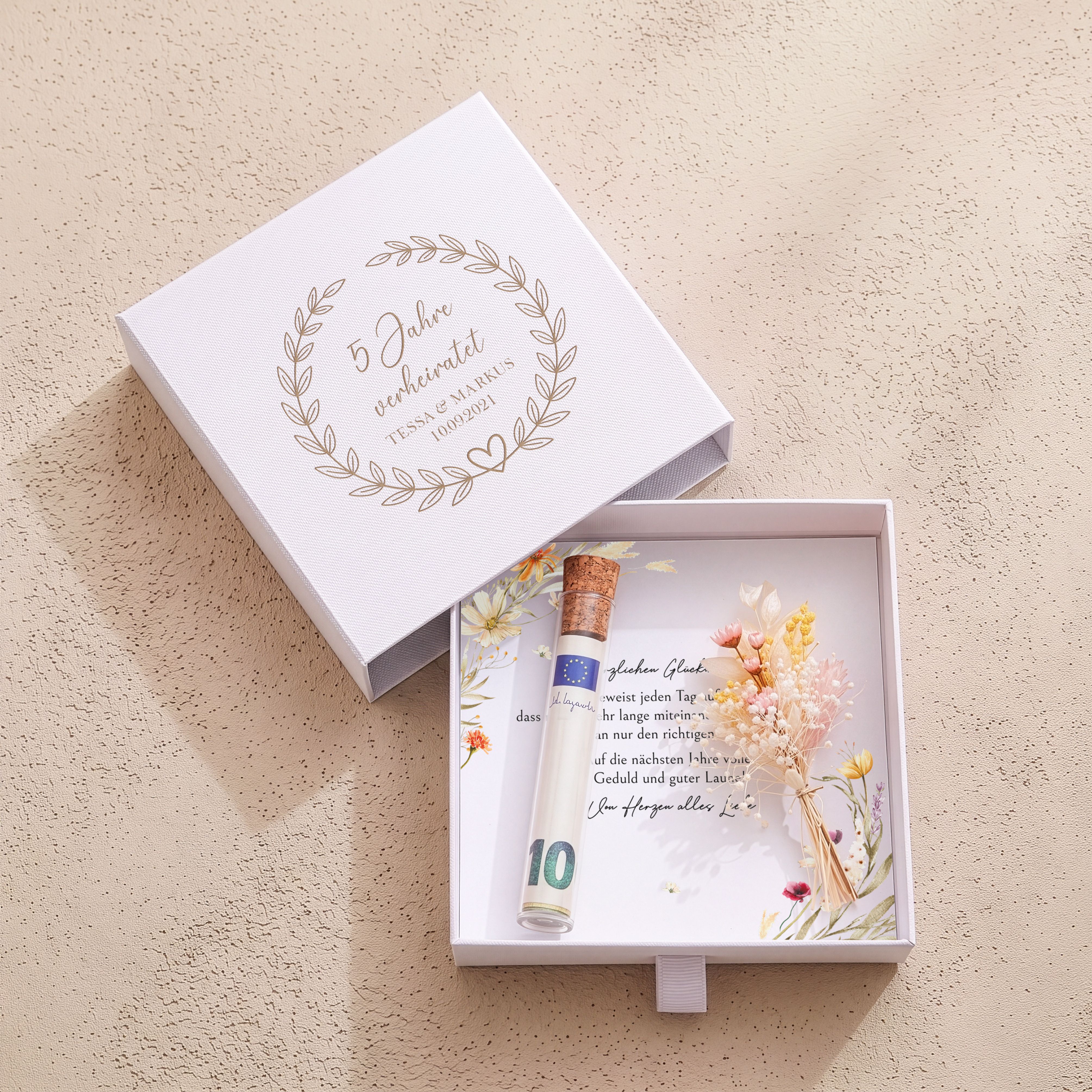 Weiße Geschenkbox mit Blätterkranz für den 5. Hochzeitstag. Mit floraler Einlegekarte, Röhrchen und rosa-gelben Trockenblumen.