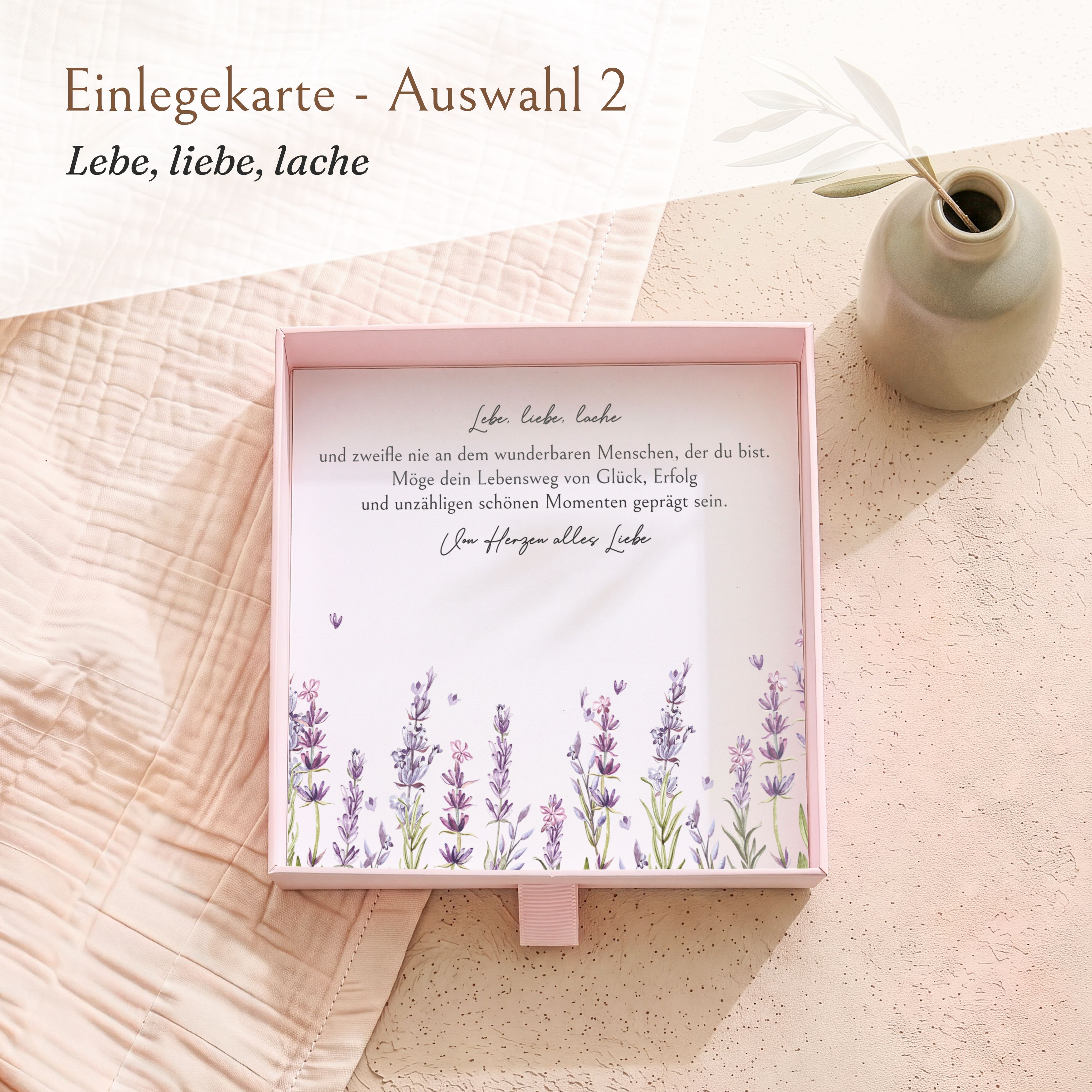 Rosa Geschenkbox aus strukturiertem Karton für Firmung. Innen liegt eine bedruckte Einlegekarte mit Lavendelblumen und dem Spruch 'Lebe, liebe, lache'.