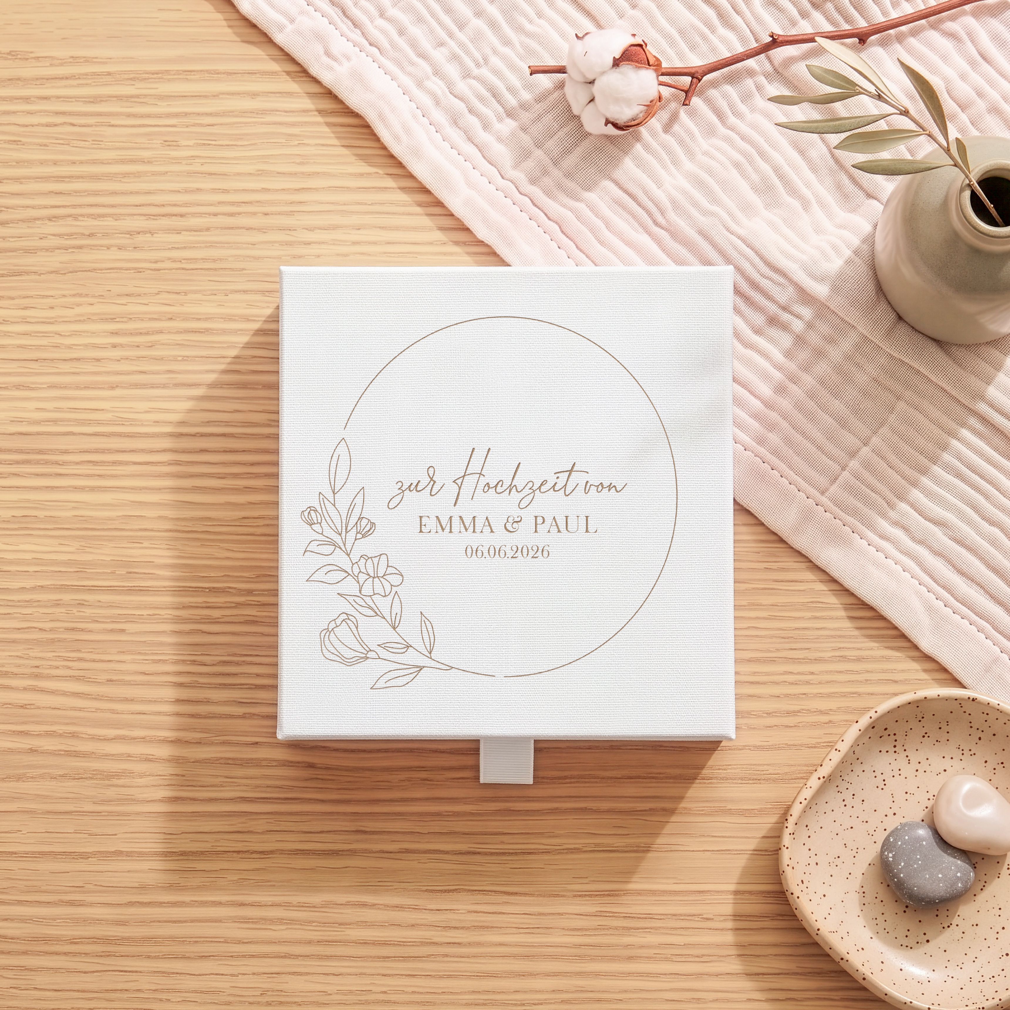 Weiße Geschenkbox aus strukturiertem Karton zur Hochzeit, mit Lasergravur eines Blütenkranzes und Platz für Namen sowie Datum.
