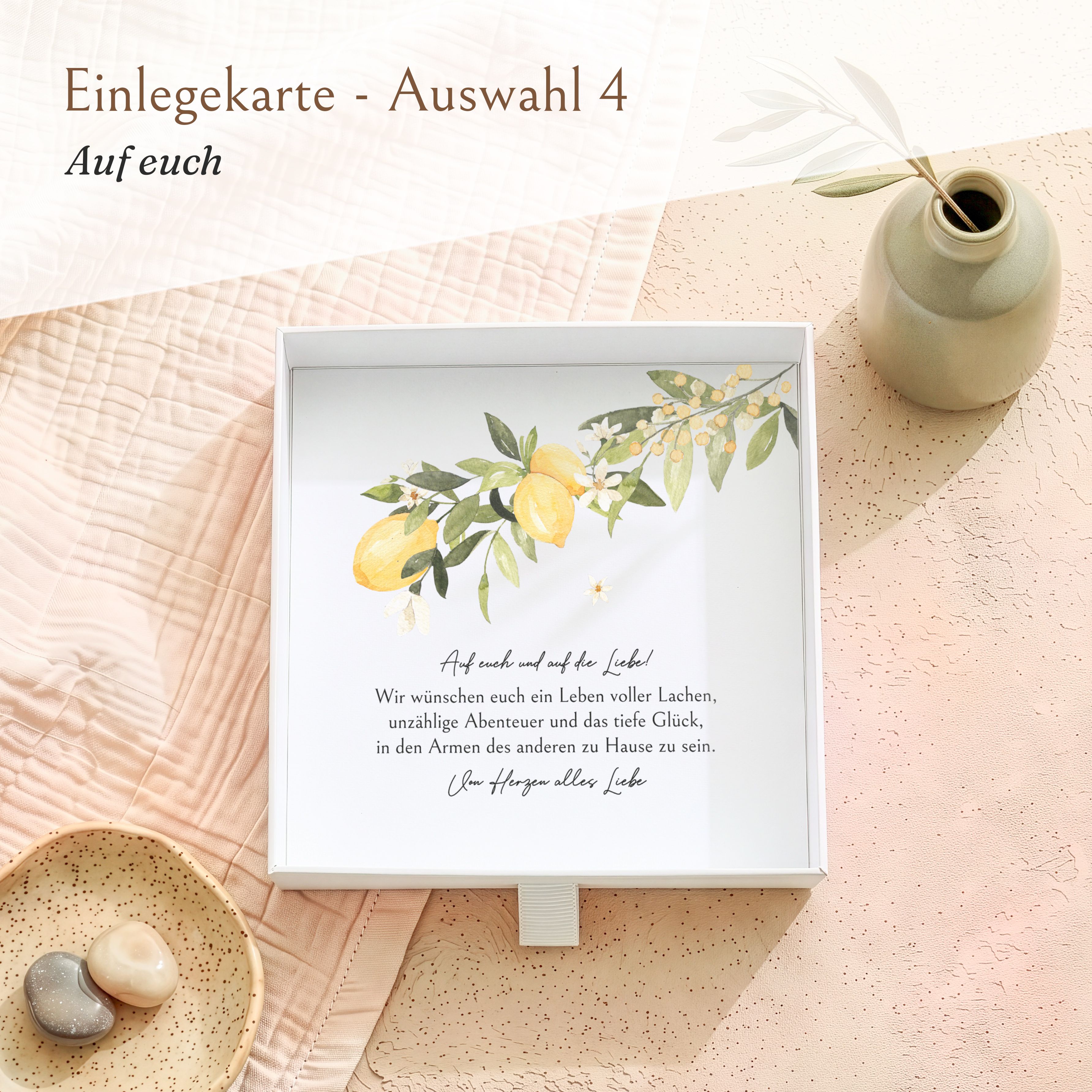 Weiße Geschenkbox aus strukturiertem Karton. Die eingelegte Karte zeigt ein Zitronen-Motiv und den Spruch 'Auf euch und auf die Liebe!'.