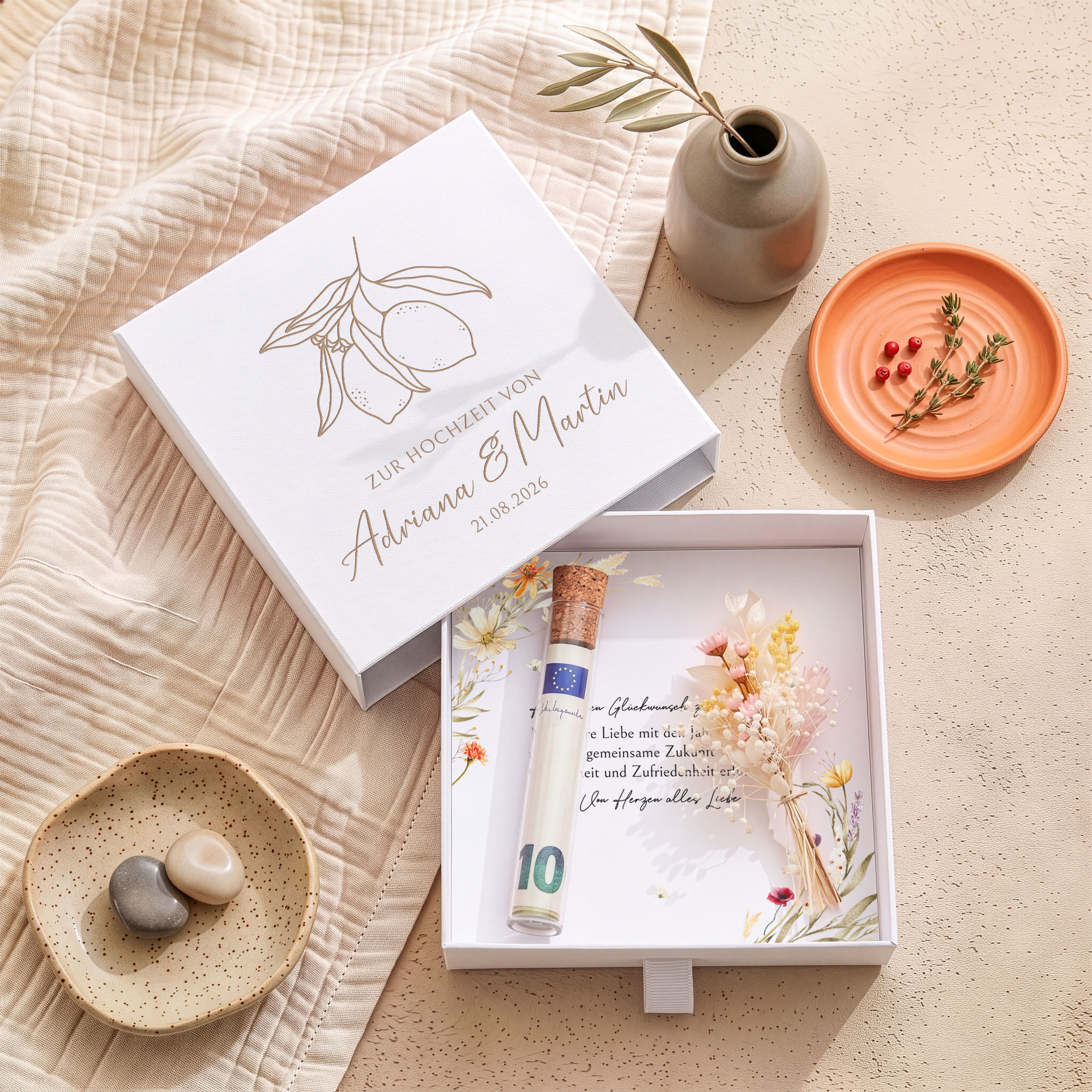 Weiße Geschenkbox aus Karton zur Hochzeit mit graviertem Zitronenmotiv und personalisierten Namen. Innen sind eine bedruckte Einlegekarte, ein Röhrchen mit Korken und ein Bund Trockenblumen sichtbar.