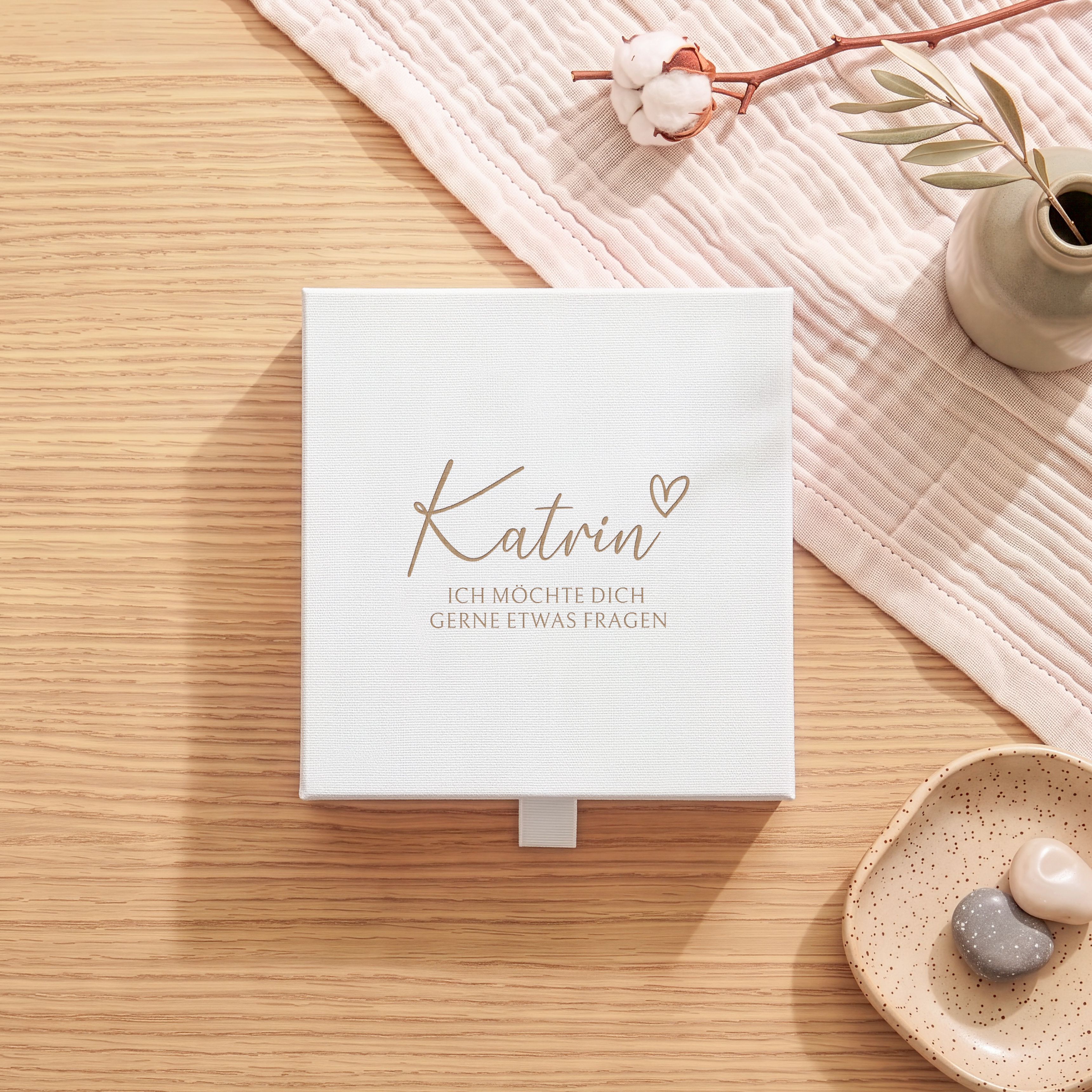 Weiße Geschenkbox aus strukturiertem Karton mit goldener Lasergravur. Das Design zeigt einen Namen mit kleinem Herz und dem Text 'Ich möchte dich gerne etwas fragen'.
