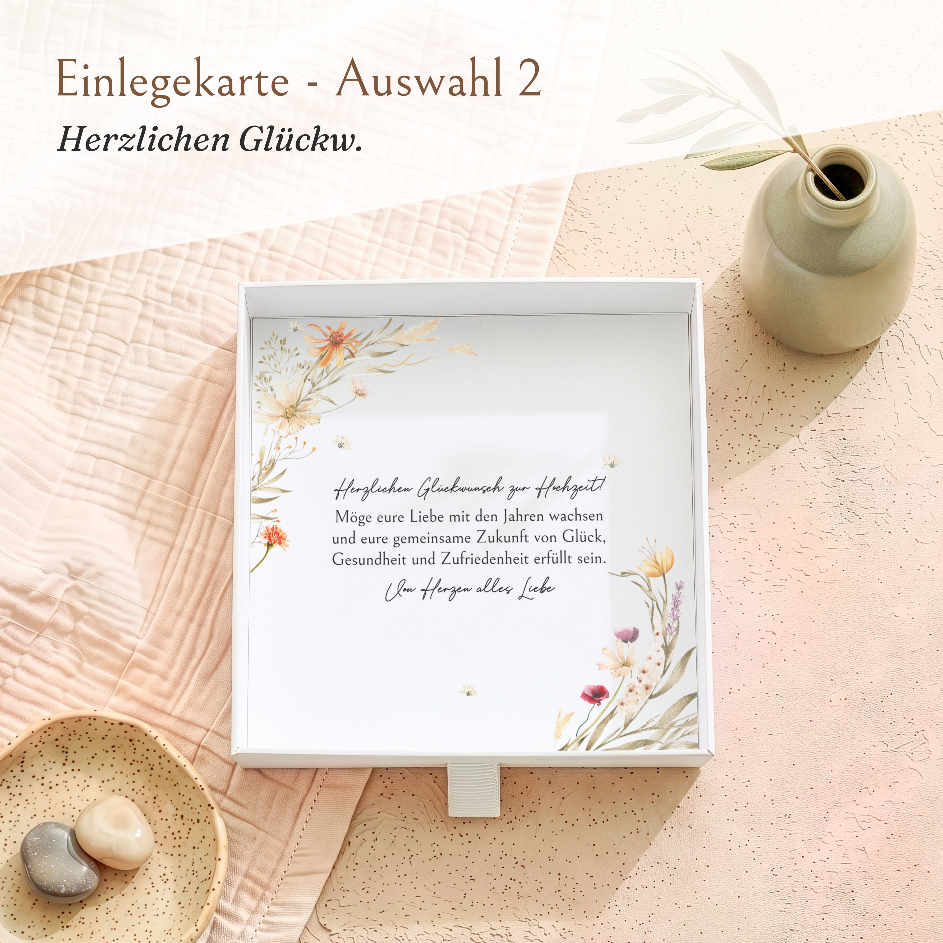 Weiße Geschenkbox aus strukturiertem Karton, geöffnet, mit bedruckter Einlegekarte. Die Karte zeigt ein buntes Blütenkranz-Motiv und einen Glückwunschtext zur Hochzeit.