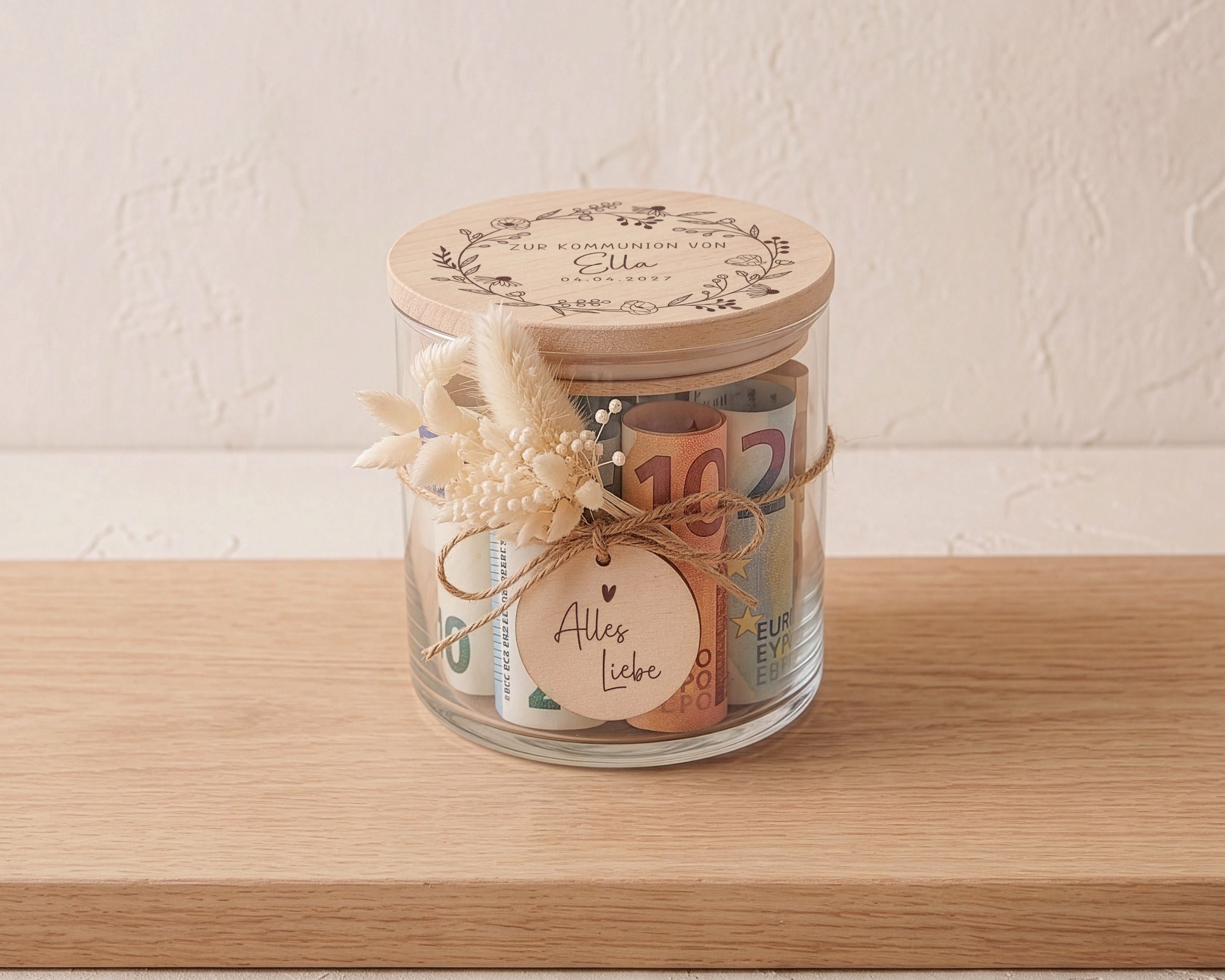 Kommunion Geschenkglas aus Glas mit graviertem Holzdeckel und Blütenkranz. Dekoriert mit beigem Trockenblumen-Sträußchen und Holztag 'Alles Liebe'.