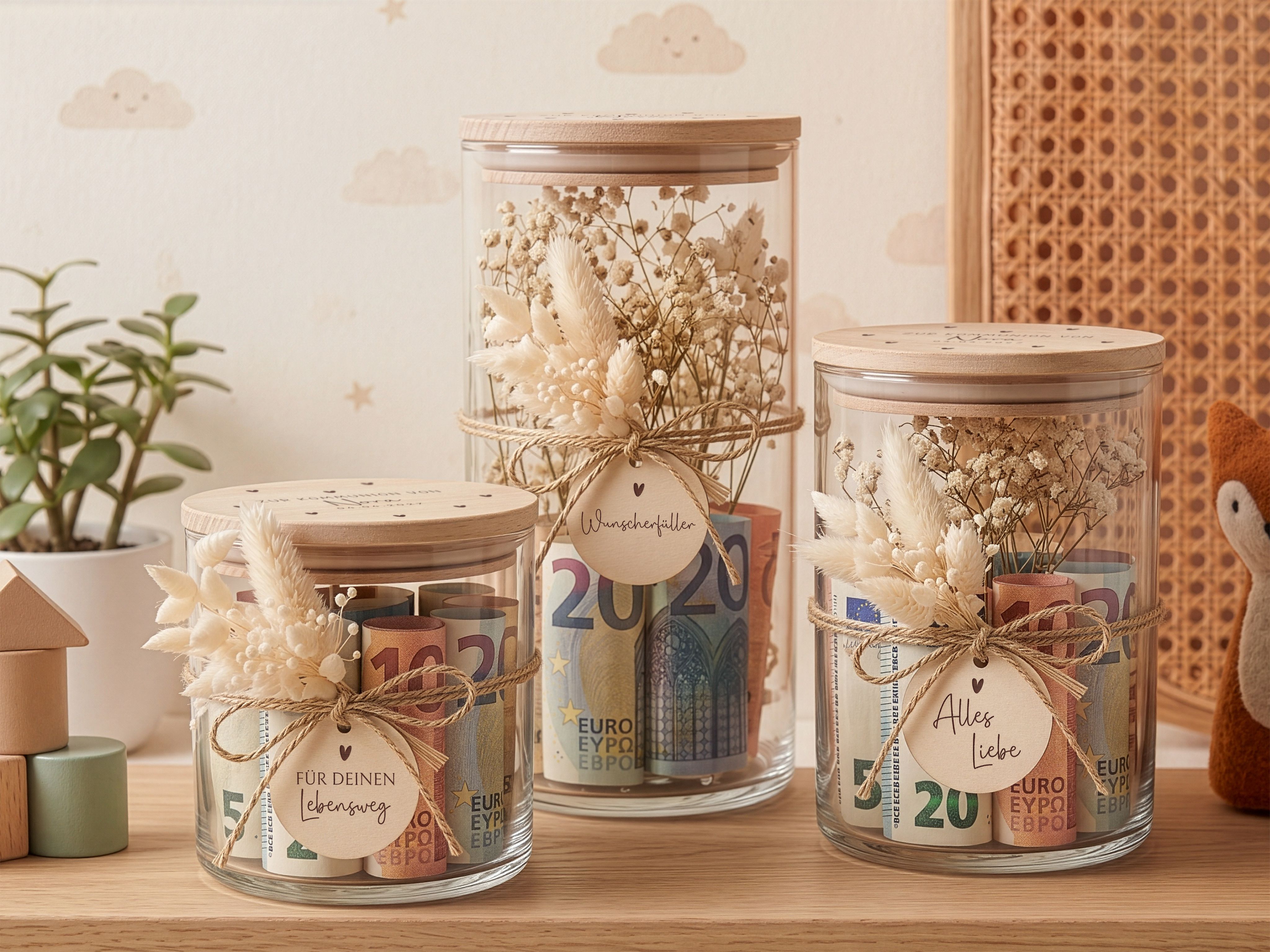 Drei Vorratsgläser mit gravierten Holzdeckeln und Herzmotiven, dekoriert mit beigen Trockenblumen und personalisierten Anhängern.
