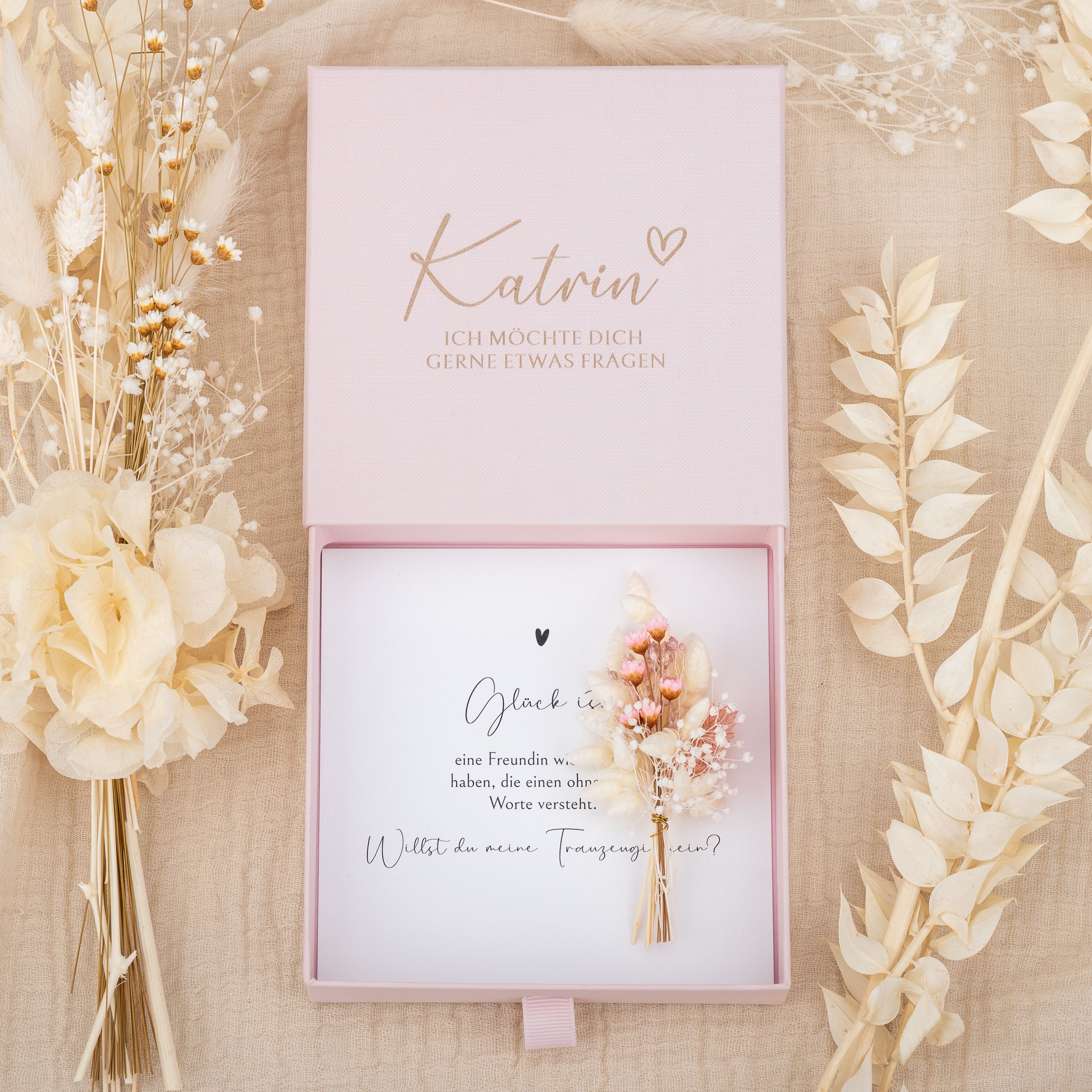 Personalisierte rosa Kartonbox mit Lasergravur Katrin und Trauzeugenfrage. Innen eine Einlegekarte und Trockenblumen